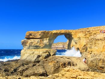 Rock formation on sea shore against clear blue sky