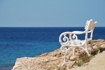 Empty bench at sea shore against clear blue sky