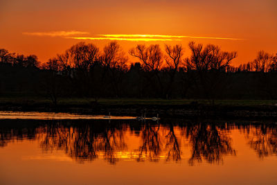 Reflection of silhouette trees in lake against orange sky