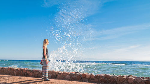 Woman standing at beach against blue sky