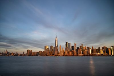 City buildings at waterfront against cloudy sky
