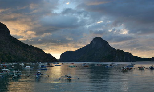 Boats in sea against mountains during sunset