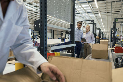 Businesswoman by businessman with engineer working in foreground at factory