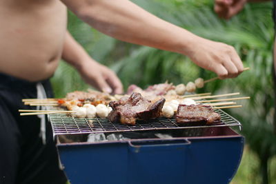 Midsection of shirtless man preparing food on barbecue grill