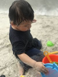 Full length of boy sitting on sand while playing with toy