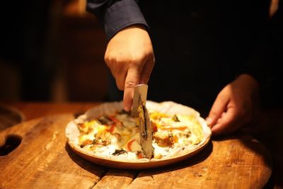 Midsection of man cutting pizza on table