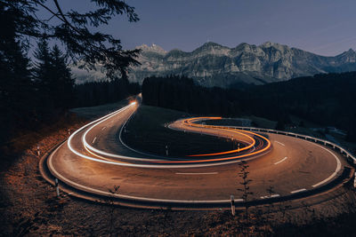 Light trails on road by mountain against sky at night