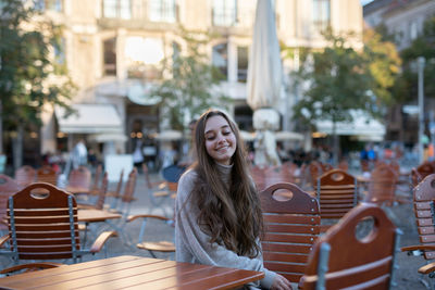 Smiling young woman sitting on seat in city