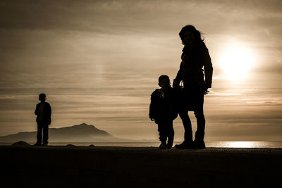 Silhouette boy standing at beach during sunset