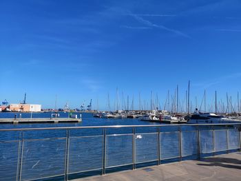 Sailboats moored at harbor against blue sky