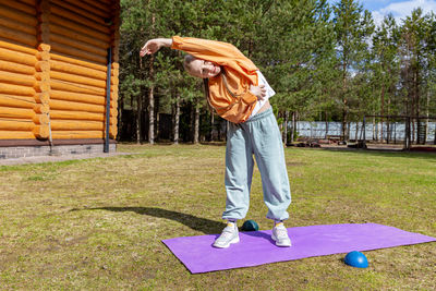 A teenage girl goes in for sports on a summer day, exercises while standing on a sports mat. 