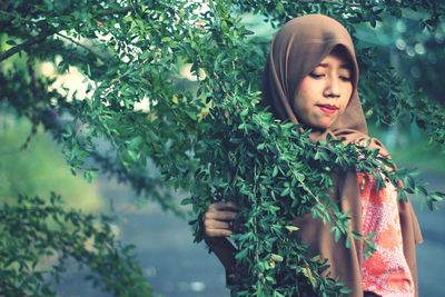 Portrait of beautiful young woman standing against plants