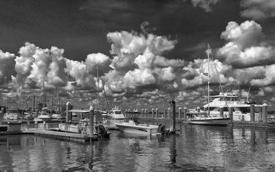 Boats in harbor against cloudy sky