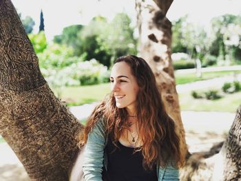 Smiling woman looking away against trees at park