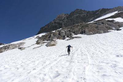 Rear view of man walking on snowcapped mountain against clear sky