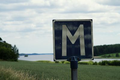 Letter m sign on grassy field against sky
