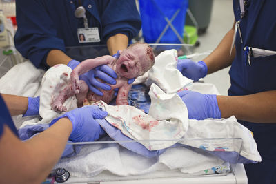 Midsection of doctors holding newborn baby boy in crib at hospital