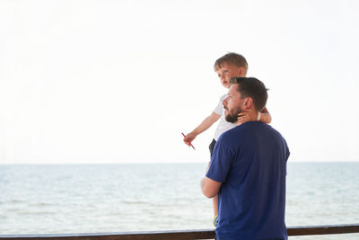 Full length of father and daughter standing at sea against sky