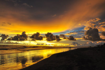 Scenic view of beach against dramatic sky during sunset