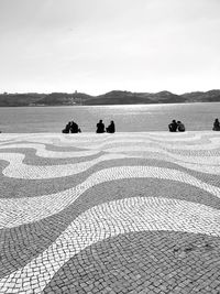 Rear view of people sitting on riverbank against sky