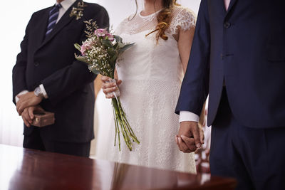 Midsection of bride and groom holding hands at church