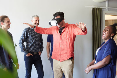 Happy business people looking at male colleague using virtual reality simulator in office