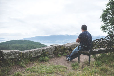 Rear view of man sitting on mountain looking at view