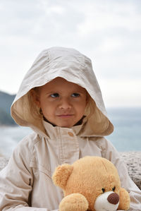 Cute girl with teddy bear standing against sea
