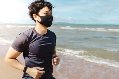 Young man standing on beach against sky