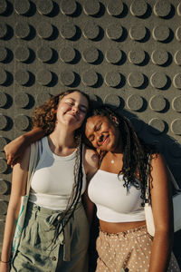 Smiling teenage girl with arm around female friend standing against wall