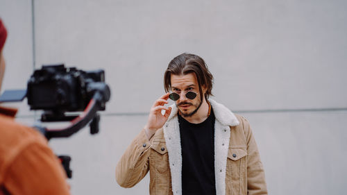 Model man looking through sunglasses and posing to the cameraman in urban street