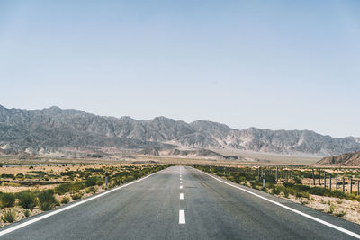 Road leading towards mountains against clear sky