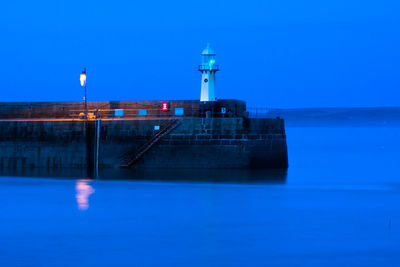 Lighthouse by sea against sky at dusk