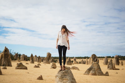 Woman standing on rock in landscape against sky