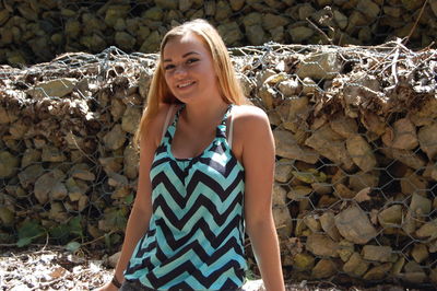 Portrait of young woman standing against pile of stones