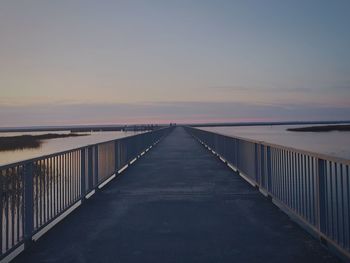 Footbridge over sea against clear sky during sunset