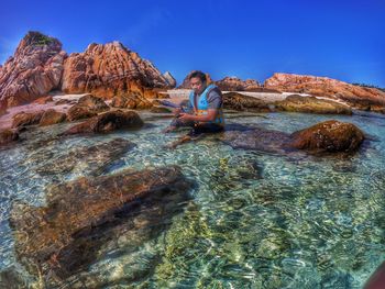 Man sitting on rock against clear blue sky