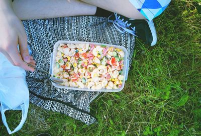 Low section of person sitting on grass, eating salad