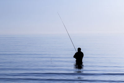 Man fishing in sea against sky