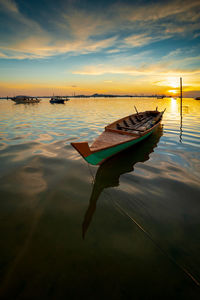 Fishing boat moored in sea against sky during sunset