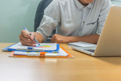 Midsection of man using mobile phone while sitting on table