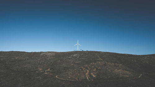 Wind turbines on landscape against clear blue sky