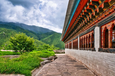 Footpath amidst buildings against cloudy sky