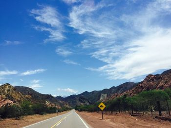 Road leading towards mountains against blue sky