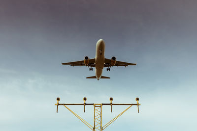 Low angle view of airplane flying over lighting equipment against sky