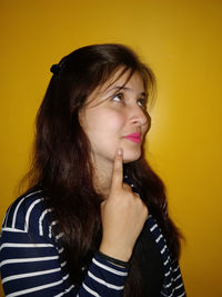 Close-up of thoughtful young woman against orange wall