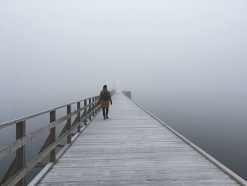 Man walking on footbridge in foggy weather against sky