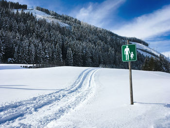 Road sign on snow covered landscape against sky