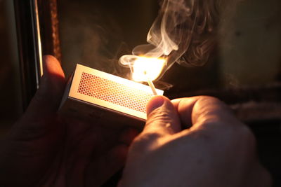 Close-up of hand igniting matchstick in darkroom
