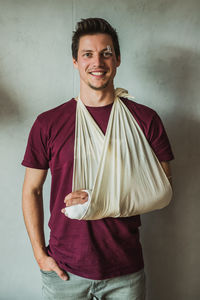 Portrait of smiling young man with fracture hand standing against wall
